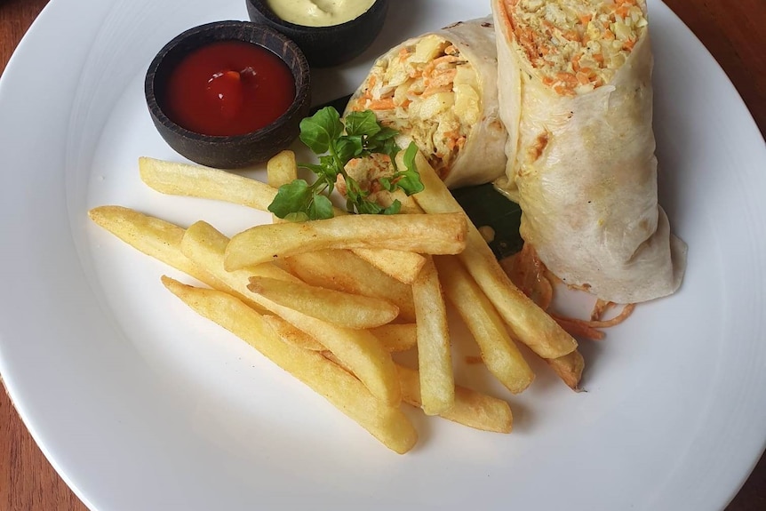 The wrap is cut in half and served with chips, tomato and mustard sauce.