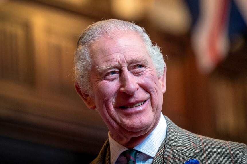 A smiling King Charles looks over his shoulder while dressed in a suit.