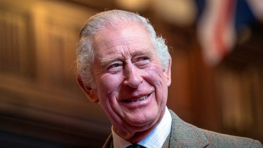 A smiling King Charles looks over his shoulder while dressed in a suit.