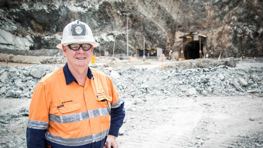 A male worker standing in open pit mine wearing hard hat