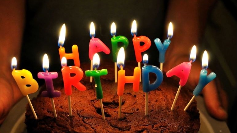 A chocolate cake with Happy Birthday candles on top lit