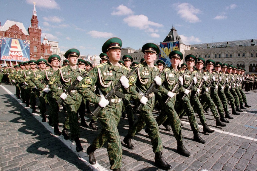 Rows of perfectly uniform Russian soldiers march holding guns in Red Square