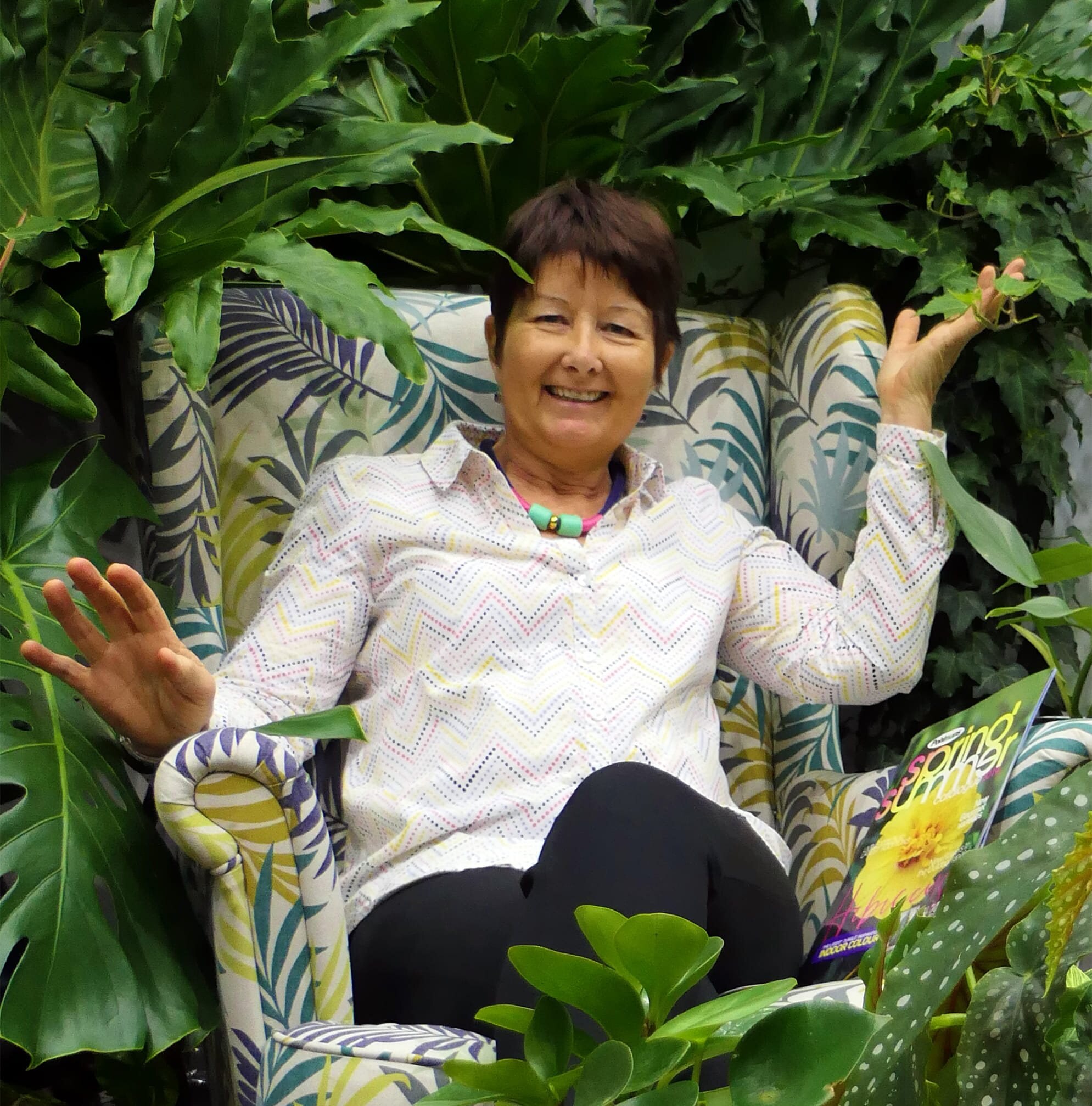 uma pessoa de camisa branca sentada em uma poltrona cercada por plantas