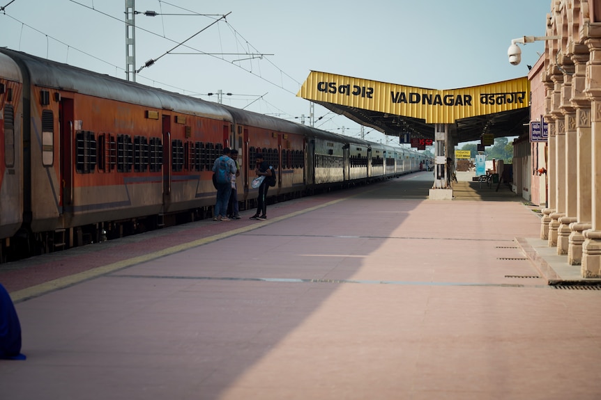 A train parked by an almost empty platform, with three people talking