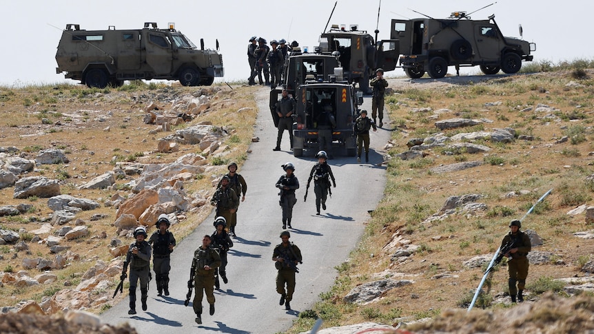 Israeli troops and trucks seen on road.