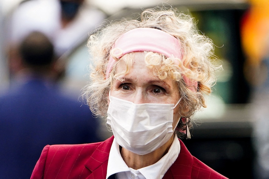 A close up of a woman with curly blonde hair wearing a face mask.