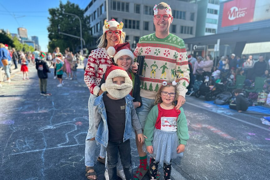 A family with three children dressed up in Christmas outfits on a street lined with people