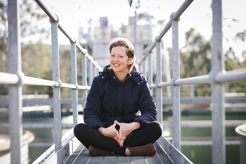 Colour photo of author Katherine Collette smiling and sitting on a mental walkway.