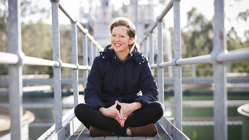 Colour photo of author Katherine Collette smiling and sitting on a mental walkway.