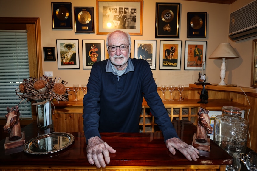 Athol Guy at home behind the bar with his awards behind him on the wall.