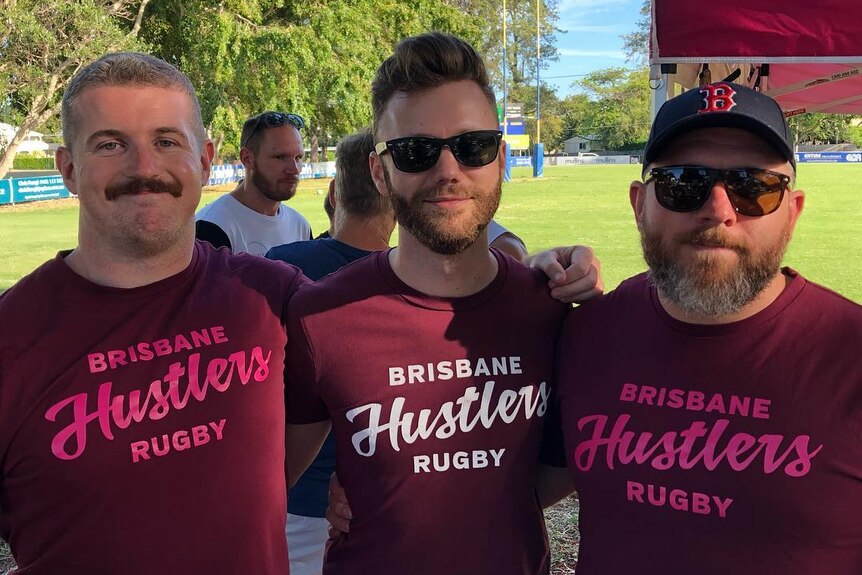 Three men dressed in maroon shirts on a rugby field.