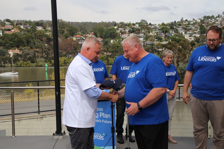 Two men wearing blue liberal shirts shake hands.
