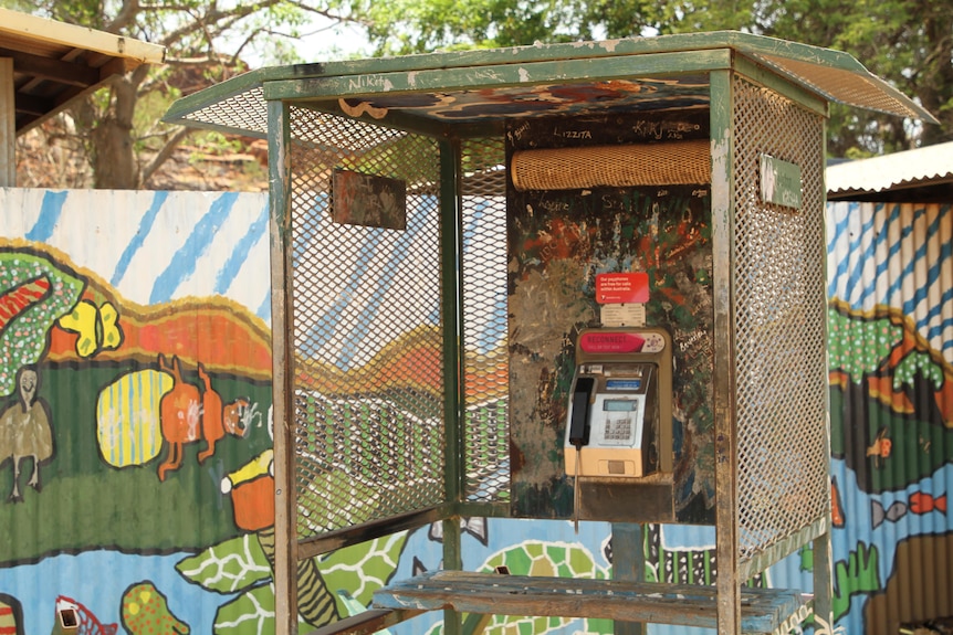 A rusty payphone booth next to a shed decorated with paintings in Looma.