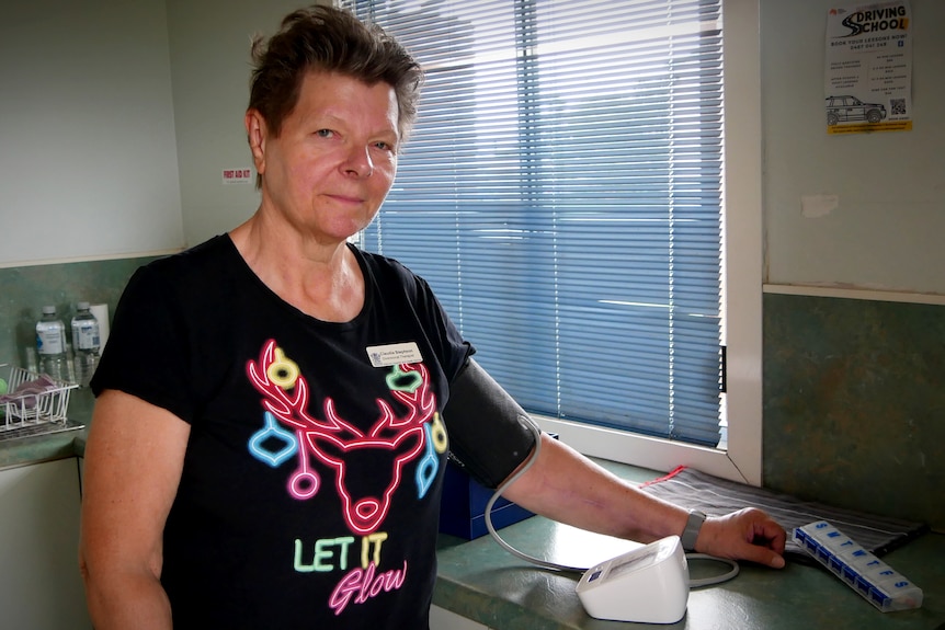 A woman wearing a black shirt with a reindeer nex to a bench with a blood pressure machine and medication