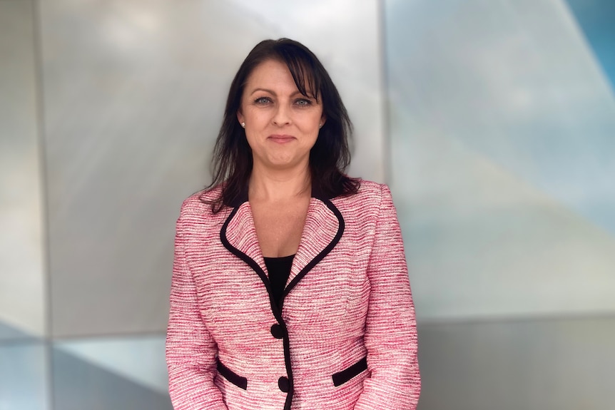 A woman with dark hair and a pink blazer smiles at the camera 