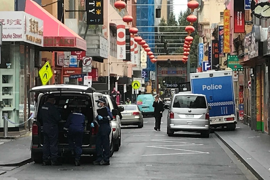Police officers wearing gloves and face masks surround a white van at a colourful part of Chinatown in Melbourne.