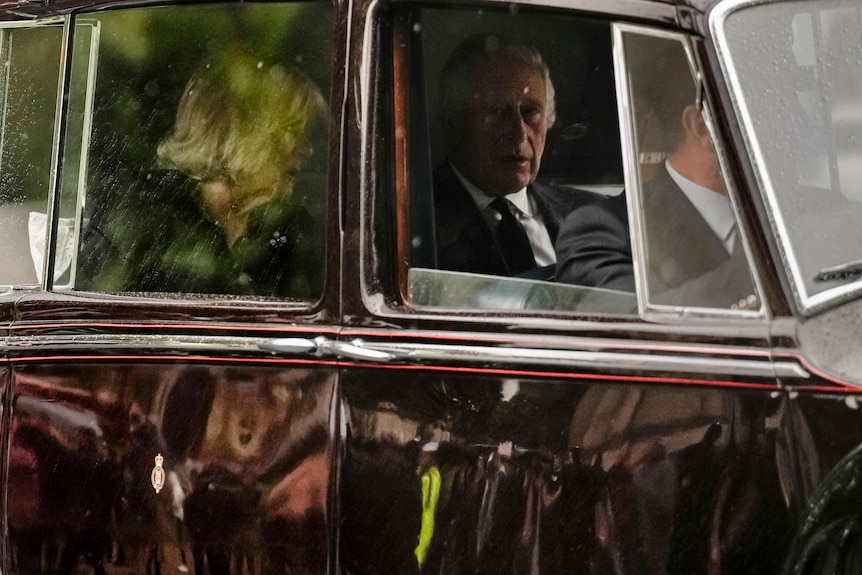 Charles apears mournful sitting inside a car with the window down. Camilla's hair can be seen through another window. 