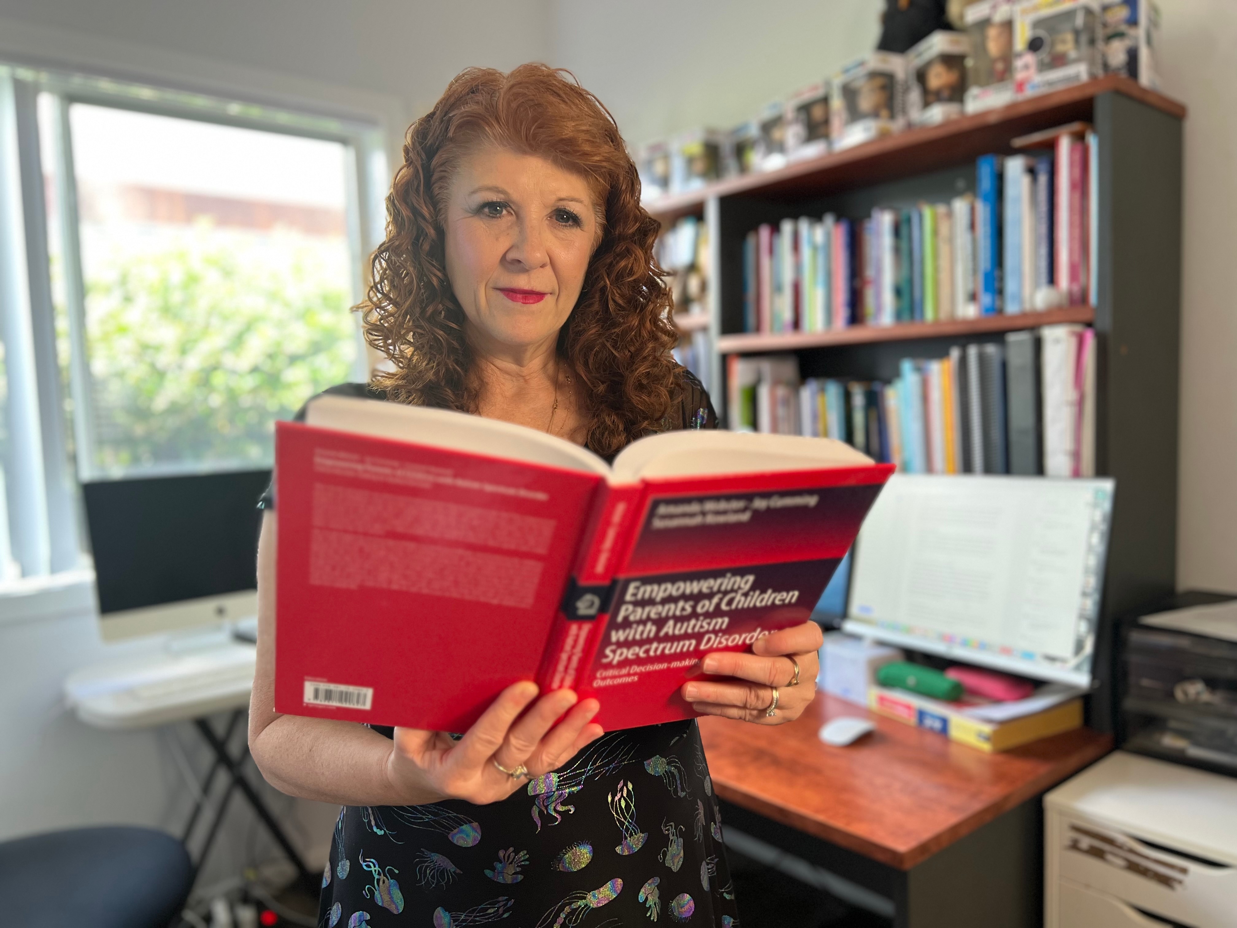 A woman with curly brown hair smiles while reading a book entitled "Empowering parents of children with autism spectrum disor