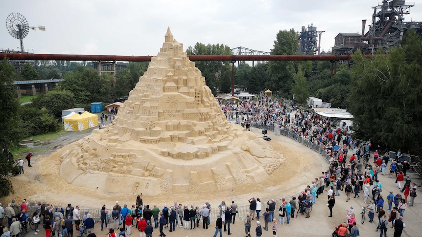 A crowd of people surround a sandcastle that has broken the record as the world's tallest.