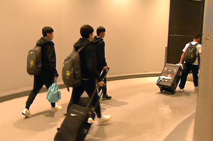 Players and support staff carry bags and pull suitcases as they walk to a hotel car park.