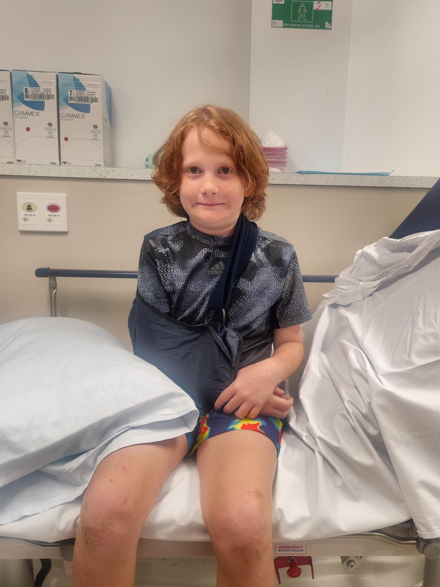 Layne sitting on a hospital bed with one of his arms in a sling.