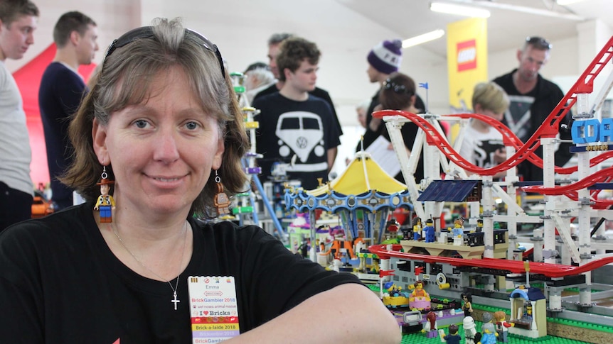 Emma leaning on a table of her Lego creations. She is smiling.