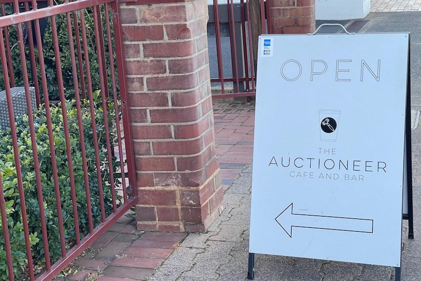 A sandwich board for a cafe reads open and points to direction of store