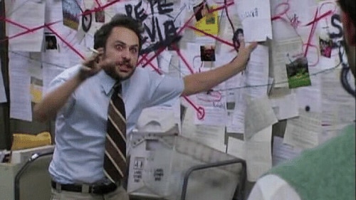 Television series character stands at a board filled with papers and connecting links