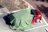 A tarpaulin over a red car in a carpark.