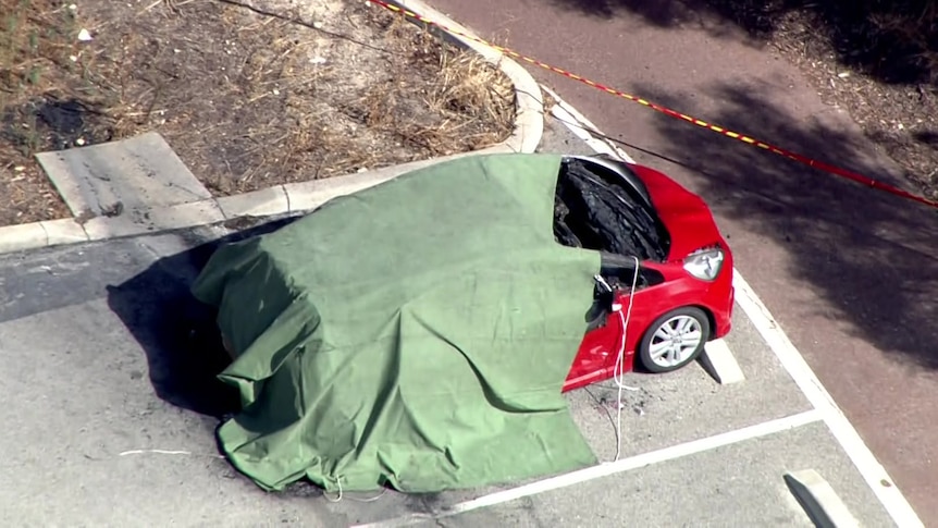 A tarpaulin over a red car in a carpark.