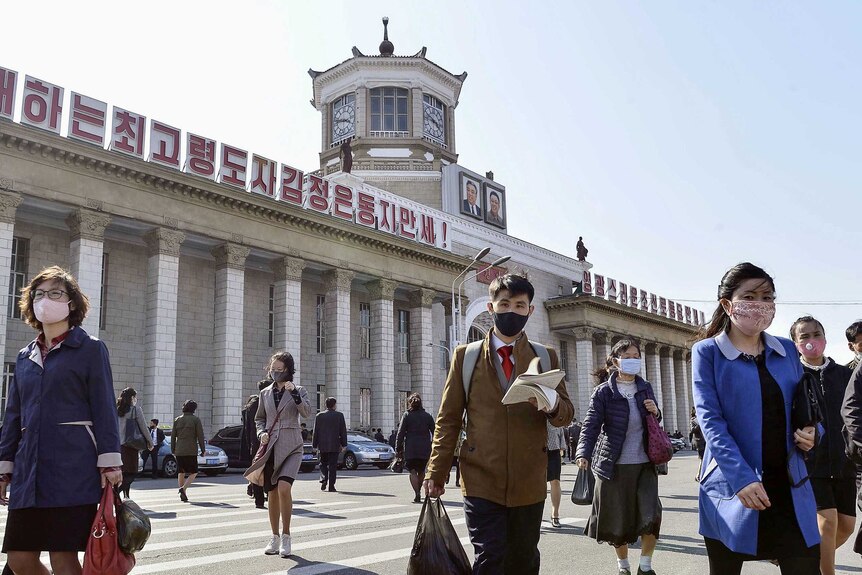 People in face masks walk outside a train station in Pyongyang
