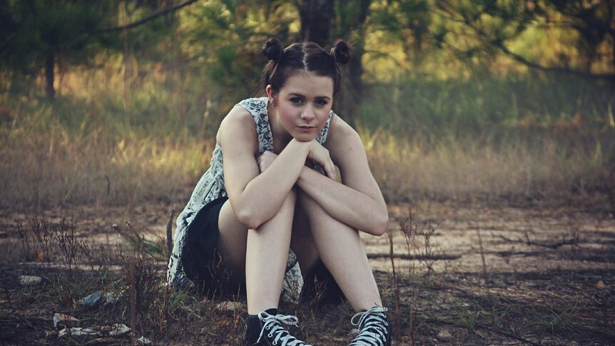 Teenage girl with hair in buns sits outside in a woodland setting