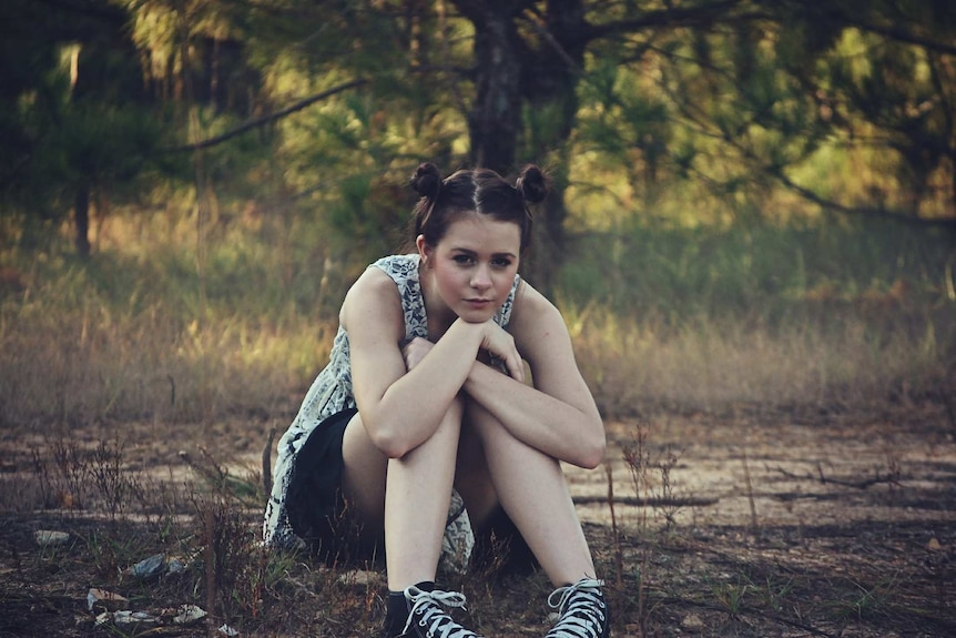 Teenage girl with hair in buns sits outside in a woodland setting