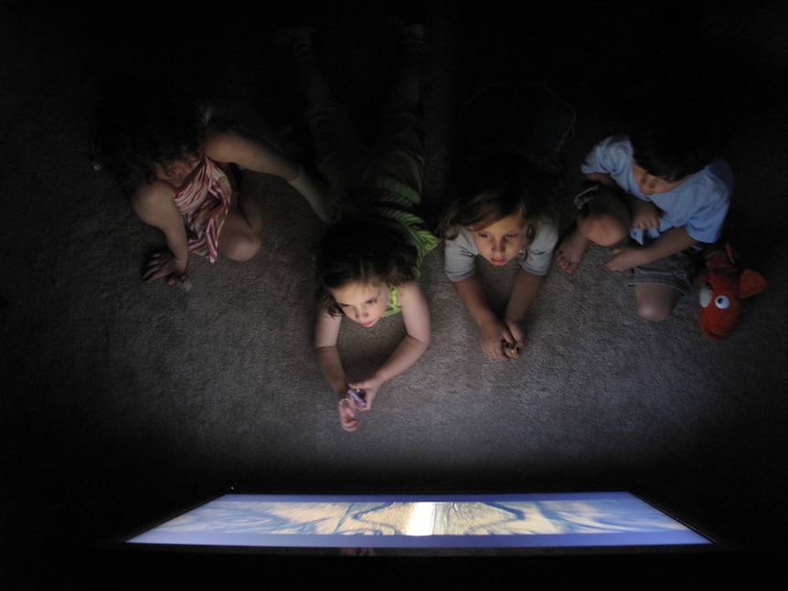 A group of children, as seen from above, watching a large TV.