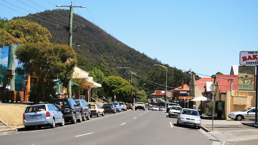 Main street of a country town, forested hill in background.