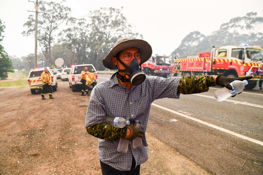 A man hands out water bottles to firefighters near Bilpin, NSW.