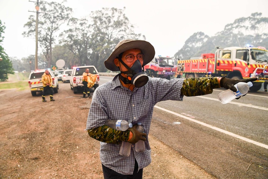 A man hands out water bottles to firefighters near Bilpin, NSW.