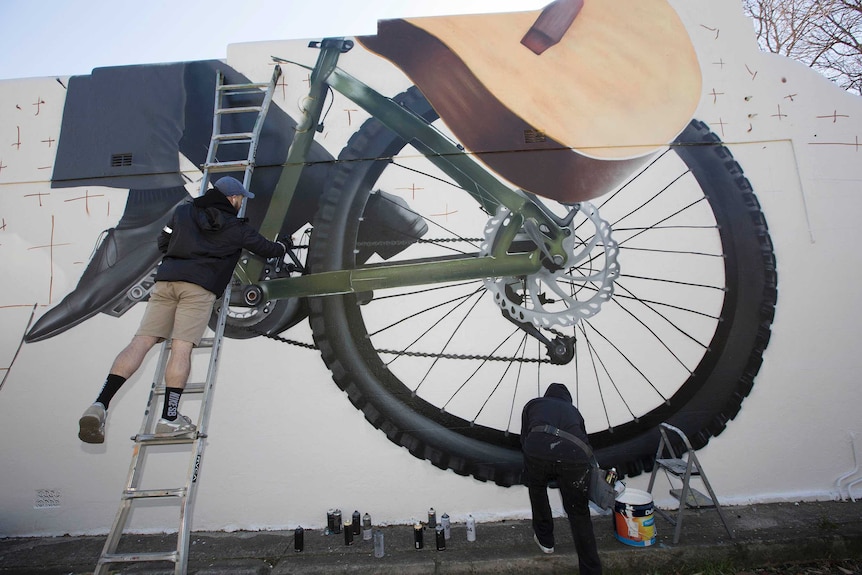 Sid Tapia working on his mural in Stanmore featuring a bike and guitar