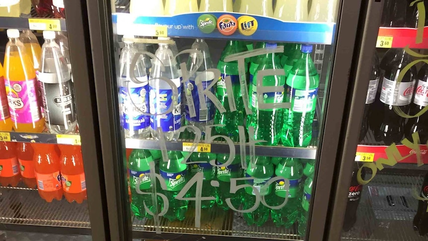Fridge of drinks with hand written sign saying $4.50 softdrink cost