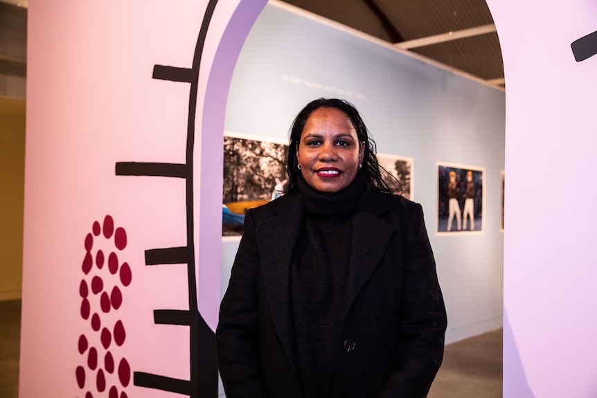 An Aboriginal woman stands in front of a pink archway in an art gallery.