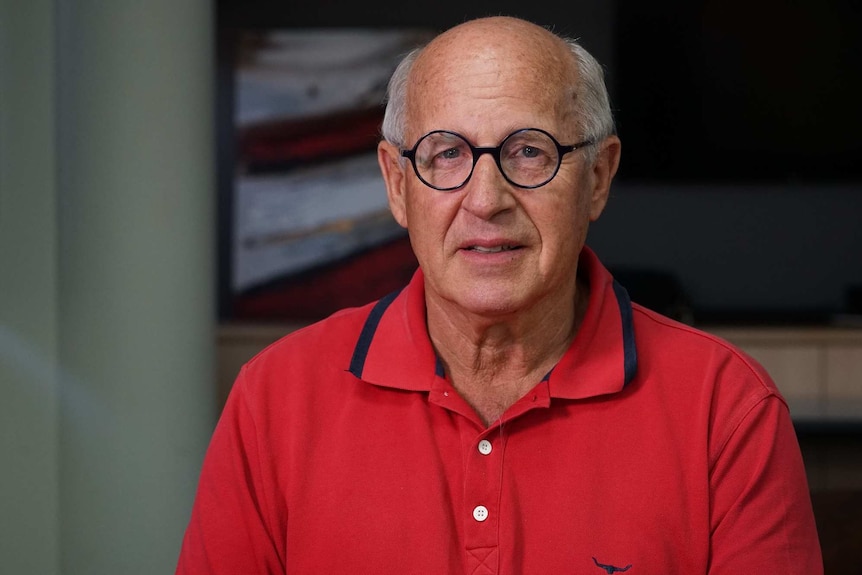 Allan McGill in a red shirt and glasses looks at the camera from close up.