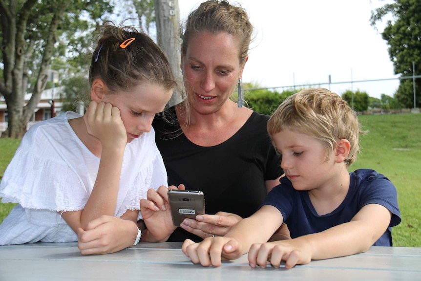 Mother-of-two Kate Perry with her children Olive and Reginald look at a mobile phone in an Ipswich park.