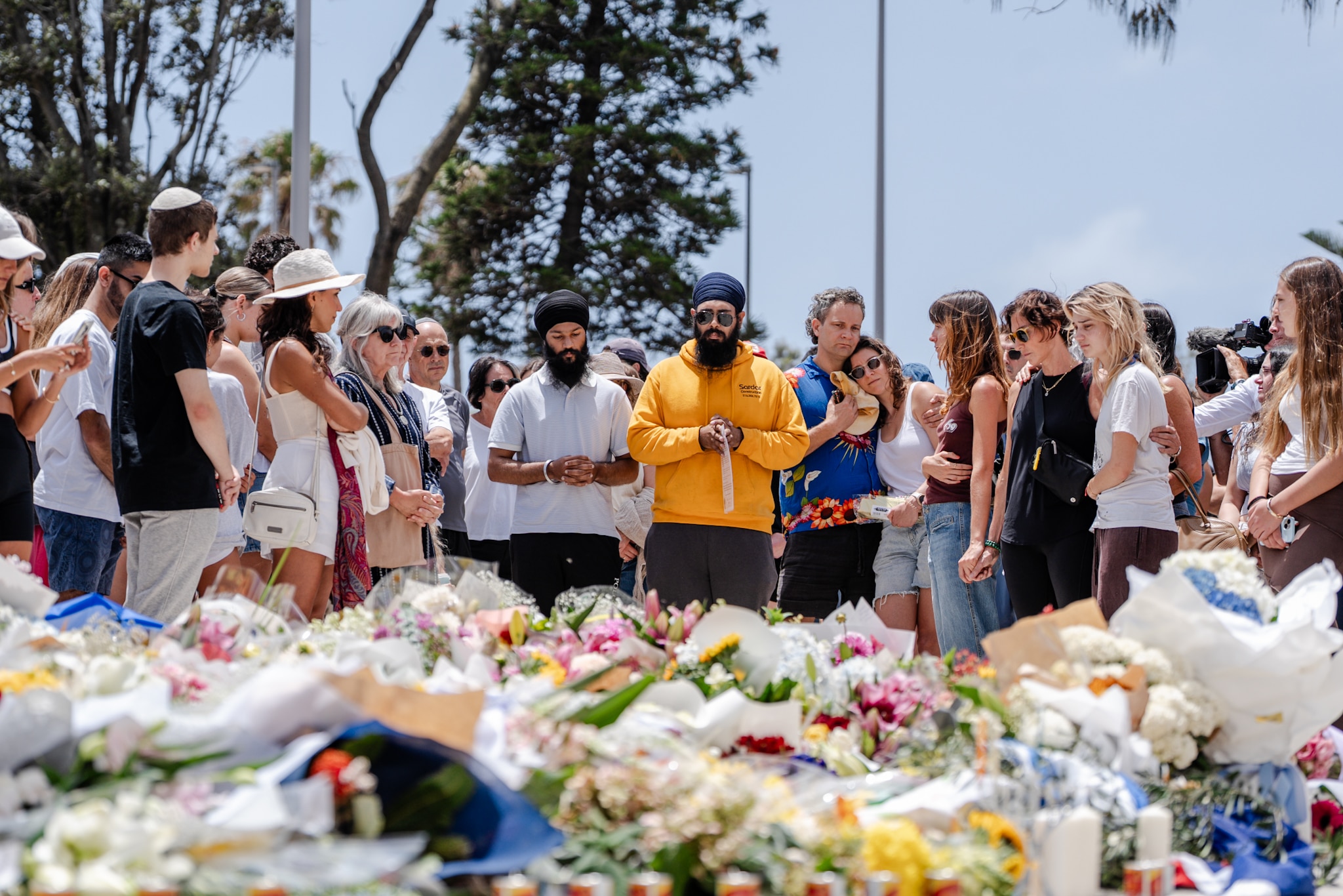 Un grupo de personas junto a un homenaje floral a las víctimas del atentado de Bondi.