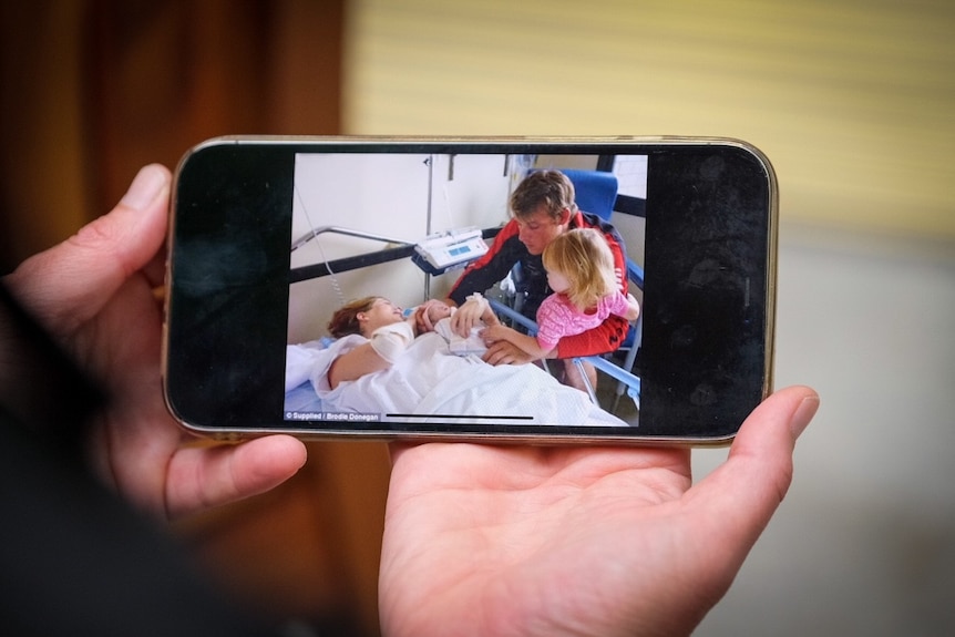 A woman holds a phone showing a picture of her in hospital