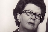 A close up sepia toned photo of Coral Bell, a woman with dark short hair in cats eye spectacles