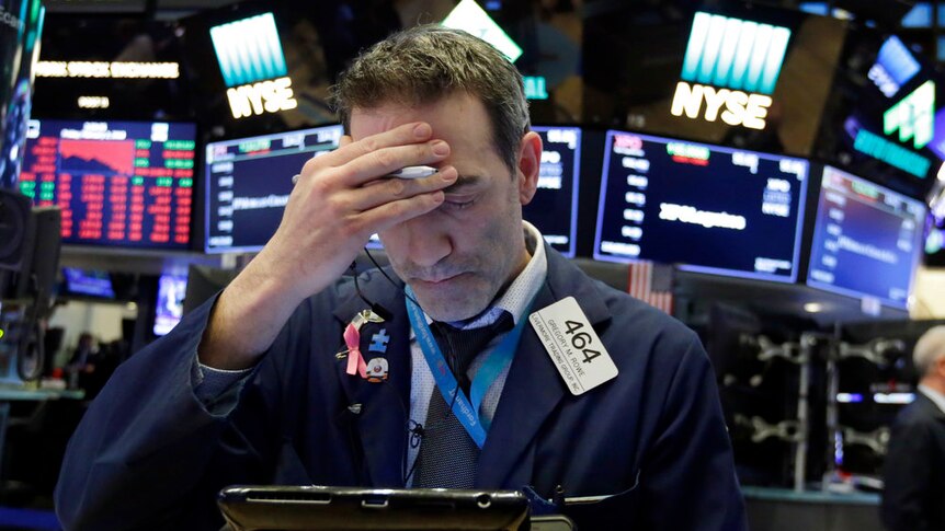 A Wall Street trader holds his head in his hand as he looks at a screen.
