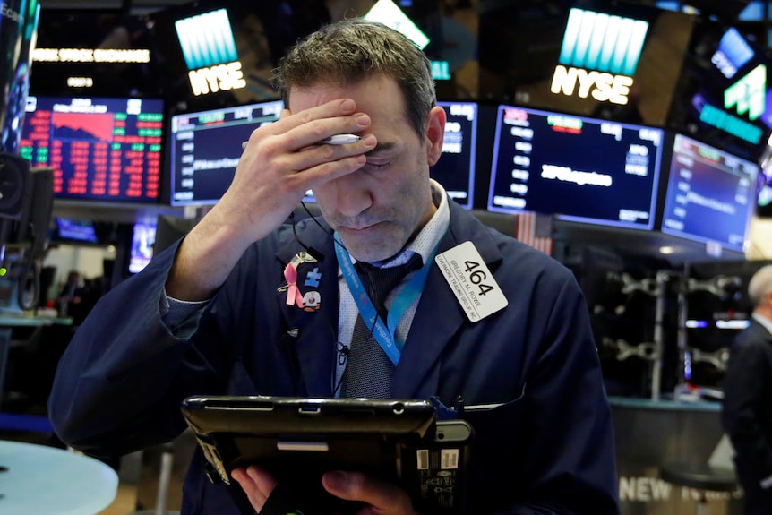 A Wall Street trader holds his head in his hand as he looks at a screen.