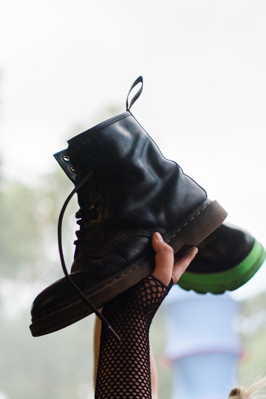 A hand in fishnets holds aloft a Doc Marten boot over a festival crowd at Golden Plains 2023