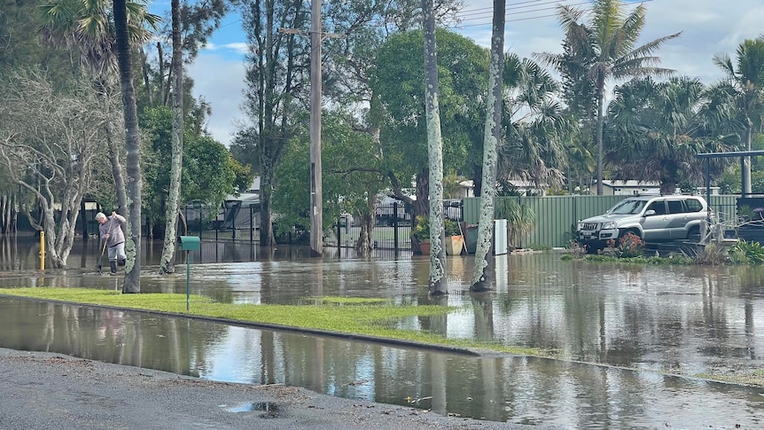 floodwaters around a home in Tuncurry with a man sweeping up