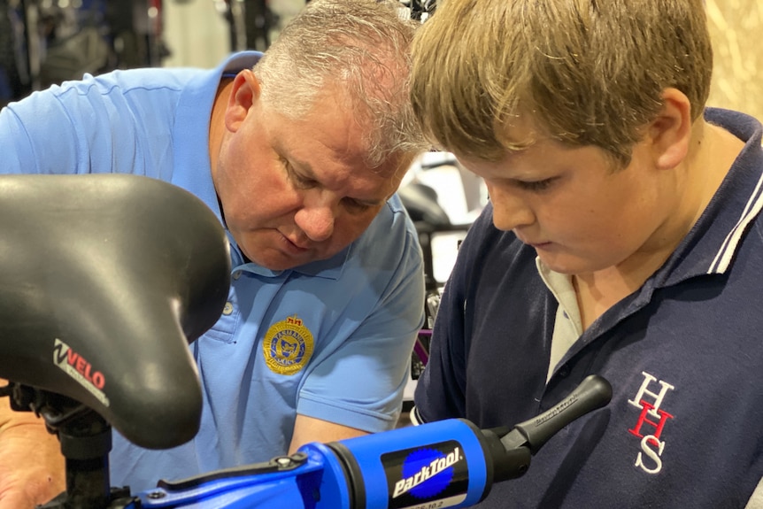 An older man helps a boy repair a bike.